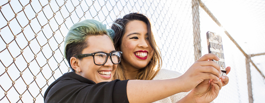 Photo of two smiling people taking a selfie outside by a fence