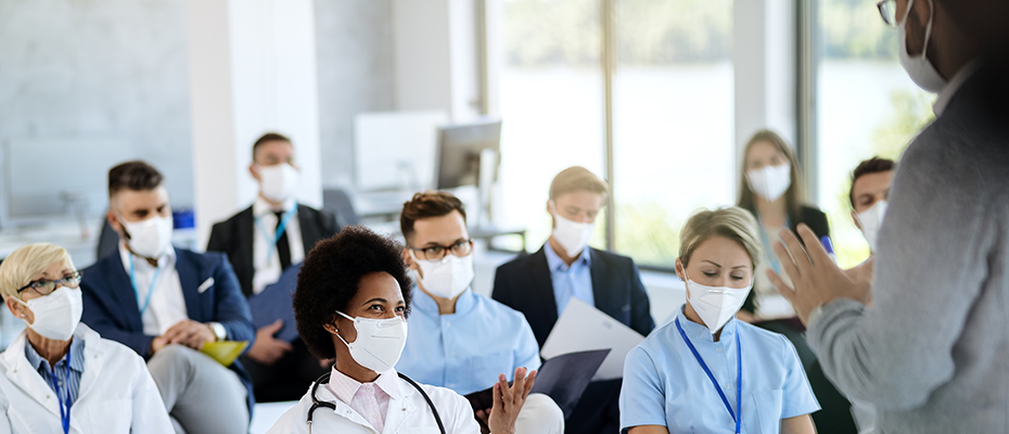 Medical students in classroom wearing masks with instructor's back in view.