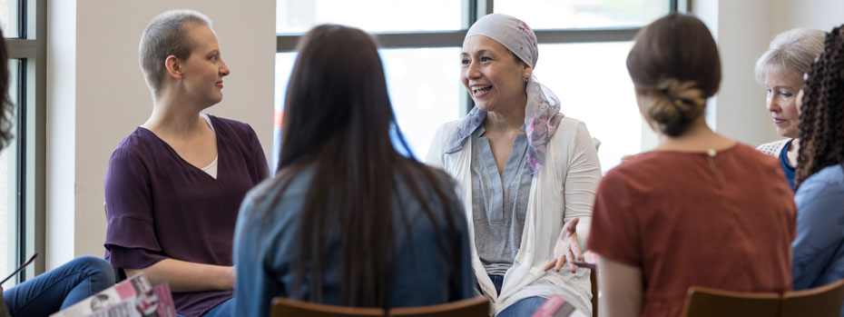 Six women are sitting in a room sharing their experience with cancer.