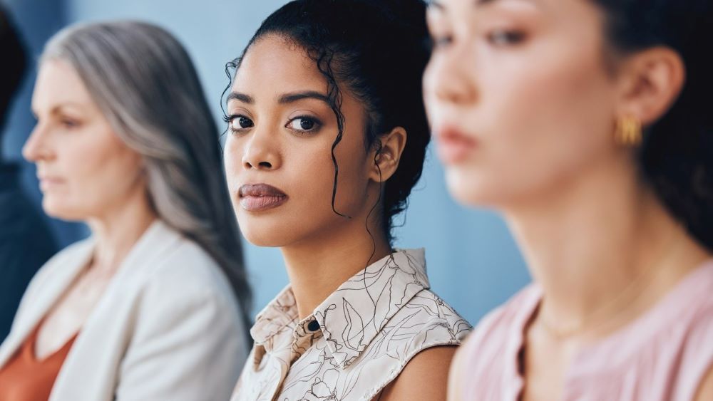 Three women sit in a line, one looking toward the camera with a serious expression.