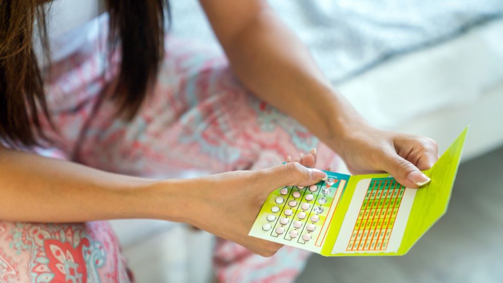 A person sits on a bed, looking at different pills in a monthly pack of birth control.