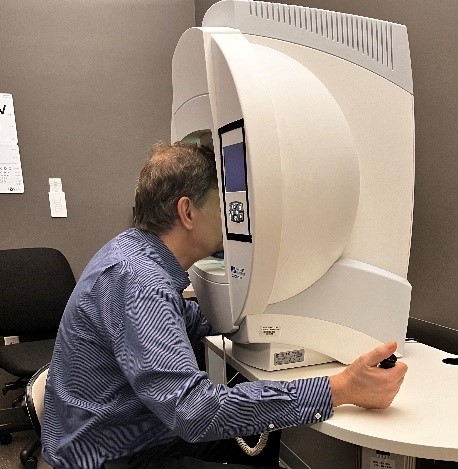 Man sits with his face inside a large white machine that tests his vision.