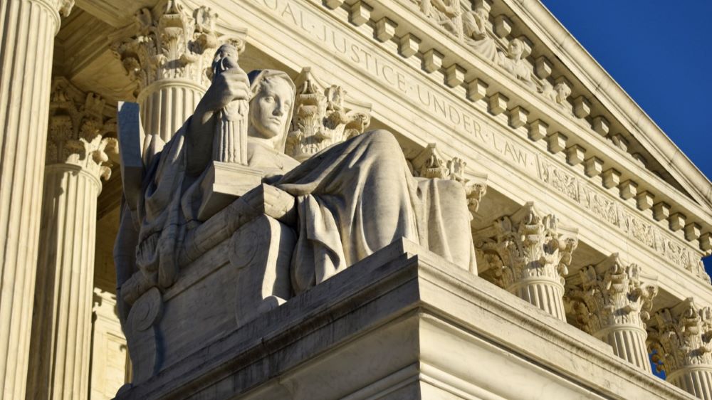 A close up shot of a statue in the foreground with the face of the U.S. Supreme Court building in the background.