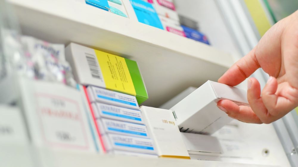 A person pulls a box of medication off a white pharmacy shelf.