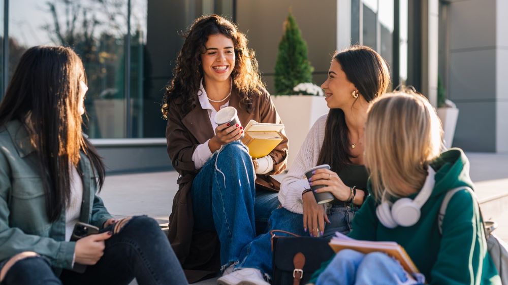 Four young adult friends sit on steps, smiling and laughing.