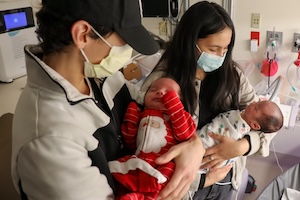 A couple wearing face masks hold their newborn twins.
