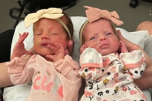 Newborn twins with large bows on their heads.