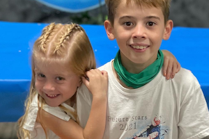 A girl with braided hair hugs an older boy.
