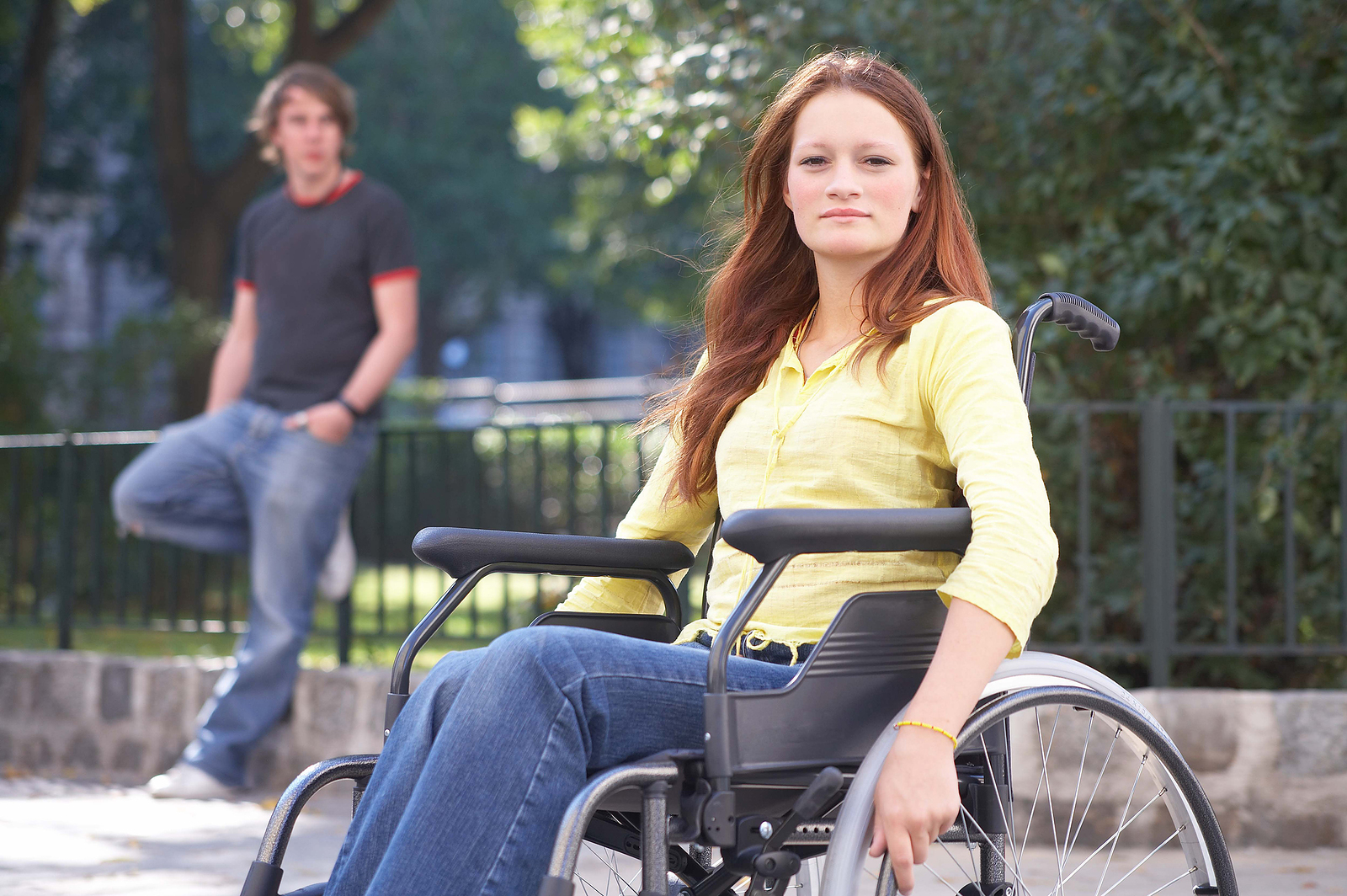 Redhaired teen in yellow shirt in wheelchair outside.