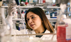 A female researcher holds up and examines a tube in a lab.