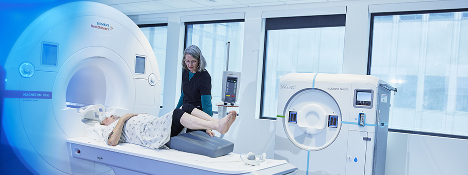 An MRI technologist at OHSU places a cushion under the raised legs of a person lying on the MRI scanner table.