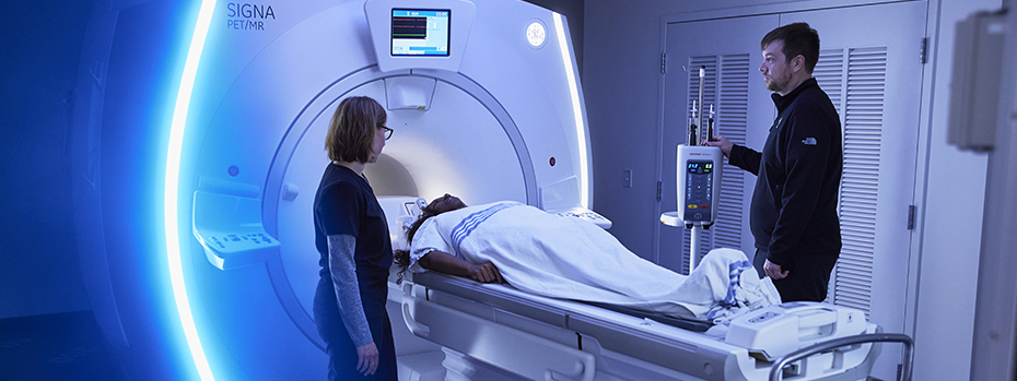 Two OHSU technicians stand on either side of a patient lying on the bed of a PET/MRI scanner in OHSU’s Lamfrom Biomedical Research Building.