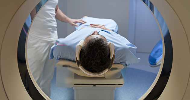 A patient lying on their back is seen through the opening of a CT scanner, head first.