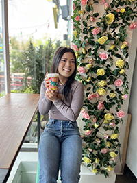 Rachel Ye holds a coffee up with a flower wall behind.