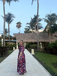 Sarah Craven standing on a paved walkway in front of palm trees and a building with a thatched roof.