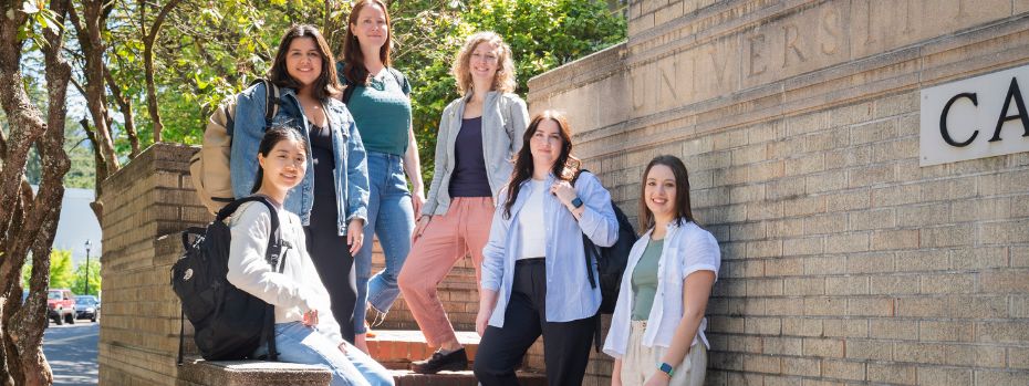 Six nursing students stand on the steps leading up to a university building and smile at the camera.