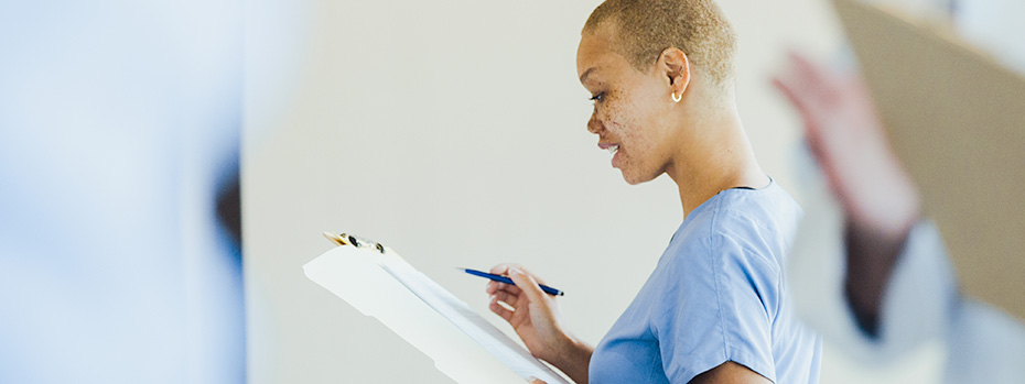 A nursing student holds a pen and a clipboard and evaluates a patient’s chart