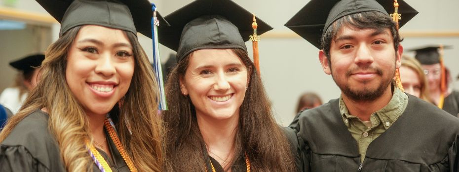 Three nursing students smile at the camera in graduation regalia