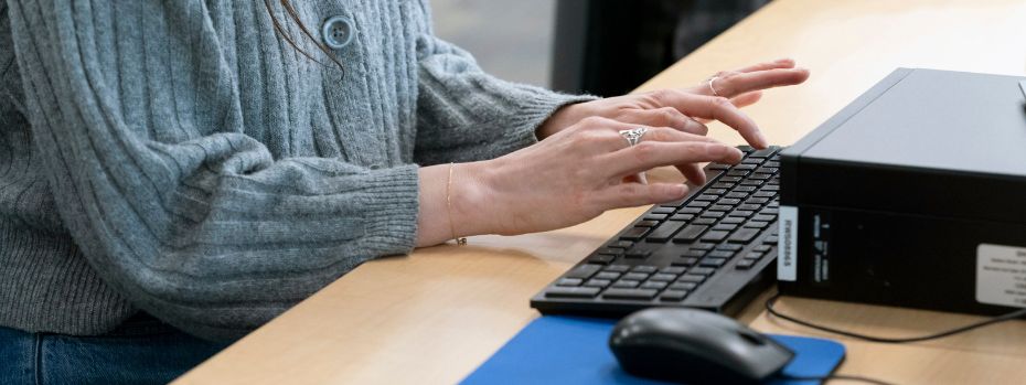 Someone in a gray sweater is sitting at a desk typing on a keyboard.