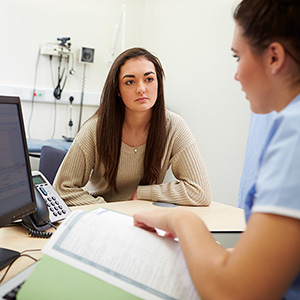 A student sits across from a doctor in an exam room.