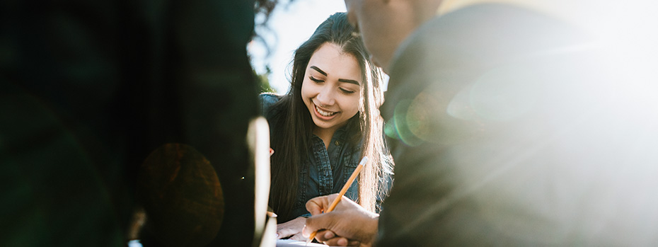 Students outdoors studying together, notebooks open, under a clear sky.