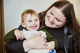 A woman holds a young boy with a cleft lip as both smile.