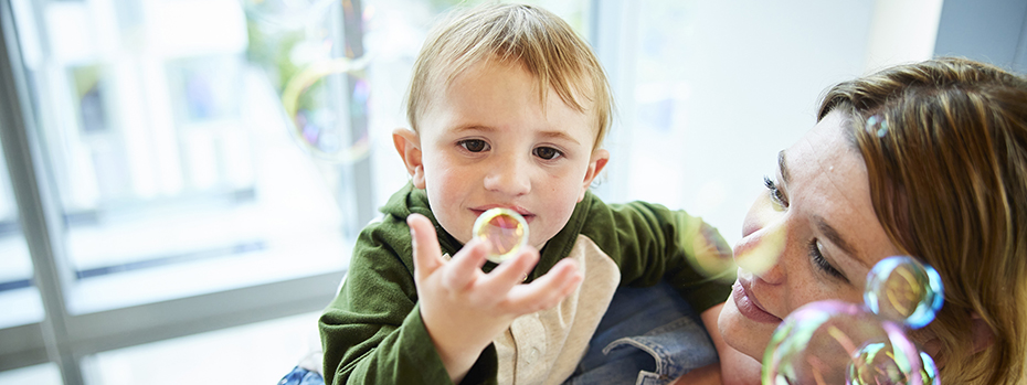 A woman holding a young boy with a cleft lip as he plays with bubbles.