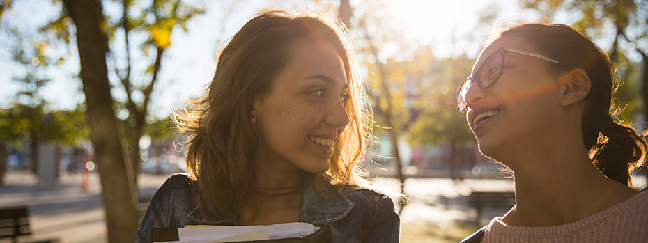 Two OHSU Klamath Falls nursing students smile at each other while walking on campus in the sunshine.