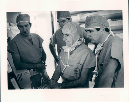 Dr. Albert Starr trains three male physicians near equipment in a surgical operating room.