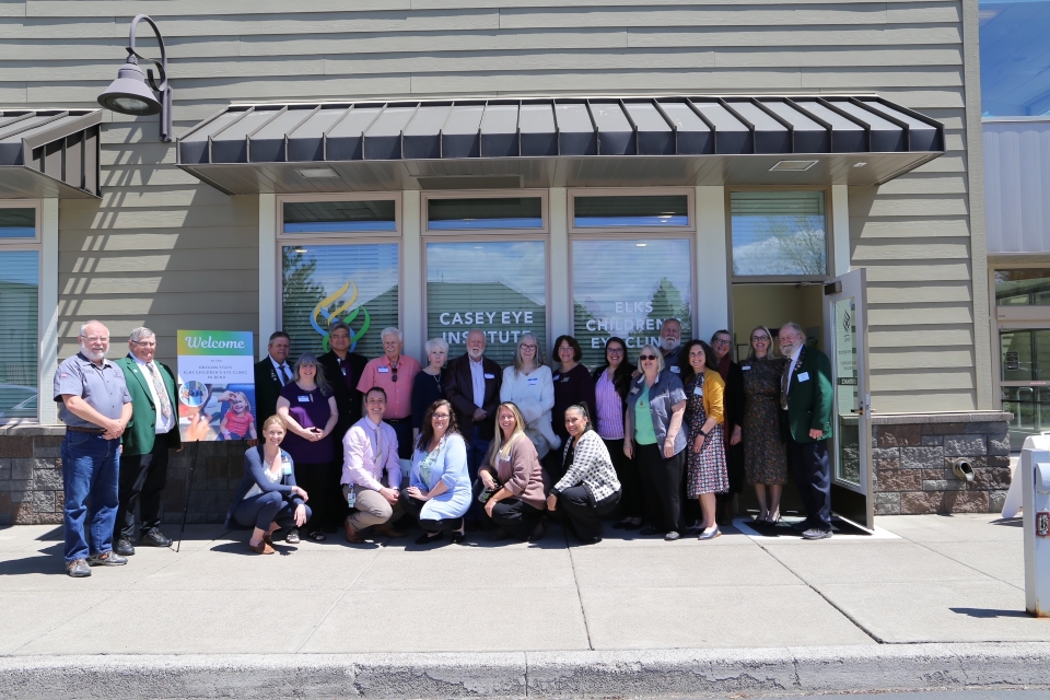 A group of people post together in two rows in front of a building entrance with the Casey Eye Institute logo sign on the window in the background.