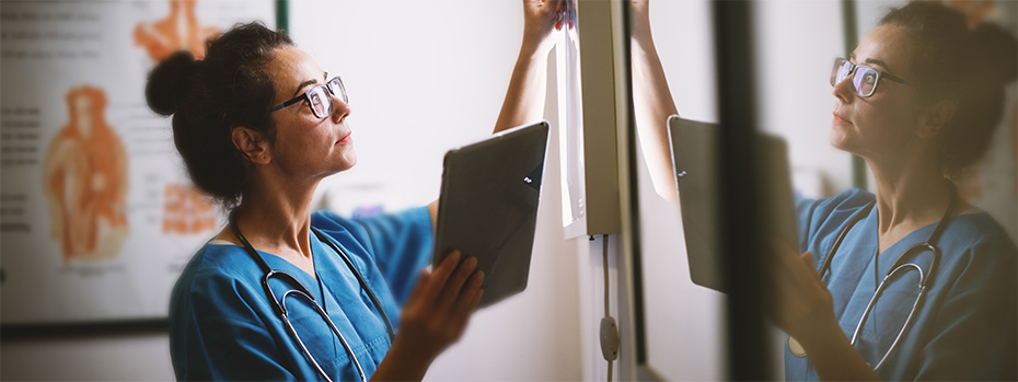 An OHSU nursing student wearing scrubs and a stethoscope reviews a patient’s chart.