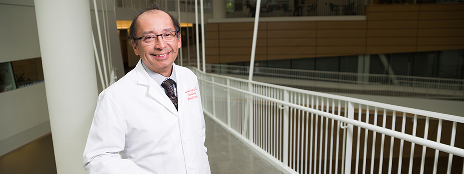 OHSU oncologist Charles Lopez smiles while standing on a mid-air corridor inside OHSU’s Robertson Life Sciences Building.