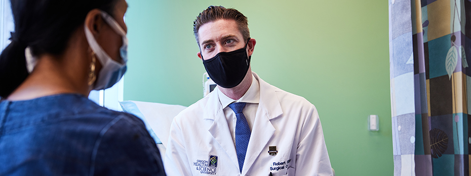 OHSU surgeon and scientist Robert Eil sits with a person in an exam room.