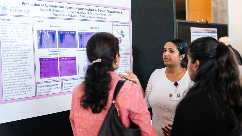 Student discusses her research poster with 2 interested people.