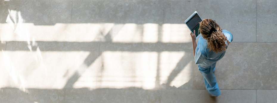 An overhead view of a nursing student in scrubs walking across OHSU’s Portland campus while holding a tablet.