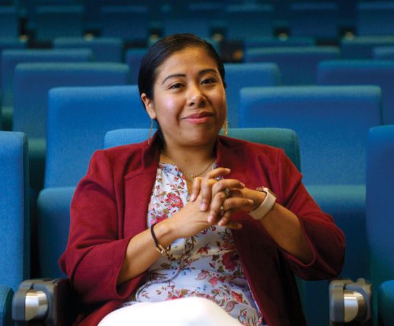 Professional portrait of Dr. Vasquez Guzman sitting in a auditorium with blue chairs.