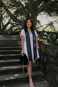 A woman stands on steps smiling on her graduation day.