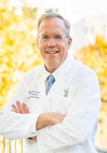 Dean Selden standing with arms crossed in front of a tree with yellow leaves