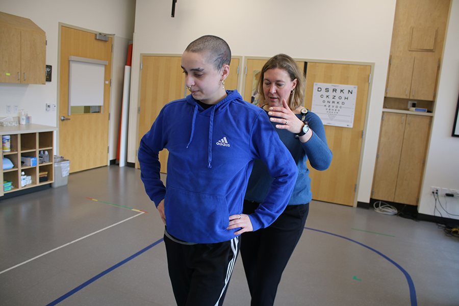 A therapist stands behind a patient as she practices balancing.