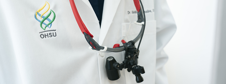 A close-up image shows a person wearing a white medical coat with the OHSU logo embroidered on it and a dental scope around their neck.