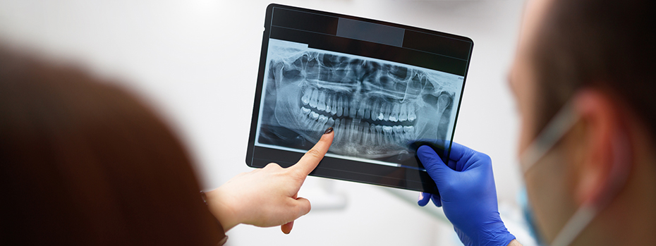 A man holds up a dental X-ray with a gloved hand while a woman standing next to him points at a tooth on the X-ray.  